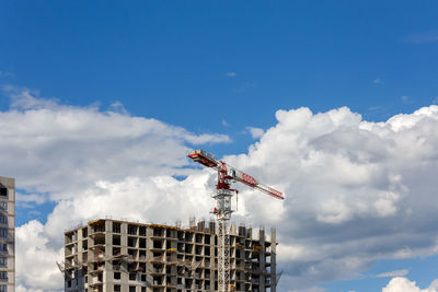 Building process of large residential apartment building with crane on cloudy sky background