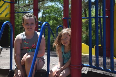 Smiling sisters sitting on outdoor play equipment