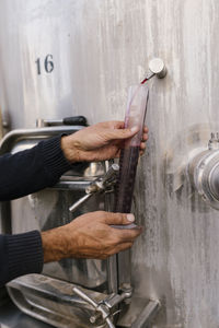 Hands of winemaker collecting red wine for examining temperature at wine cellar