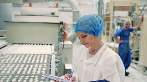 Woman writing on document while working in factory