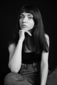 Portrait of beautiful young woman sitting against black background