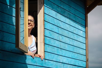 Smiling young woman looking through house window