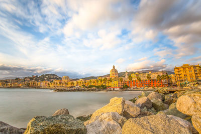 Buildings at waterfront against cloudy sky