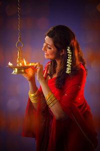 Beautiful indian woman in red sari lighting diya during diwali