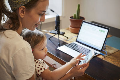 Podcaster showing mobile phone to daughter while using laptop at home