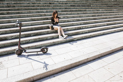 Young woman with e-scooter in the city, using smartphone