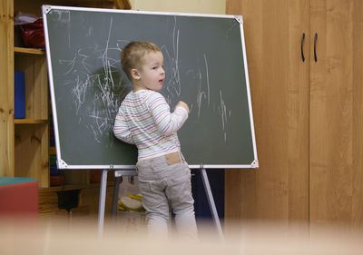 Rear view of boy writing on blackboard at classroom