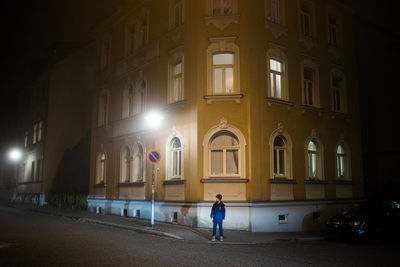 Man walking on illuminated street by building at night