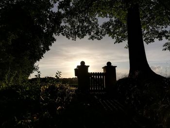 Silhouette trees at cemetery against sky during sunset