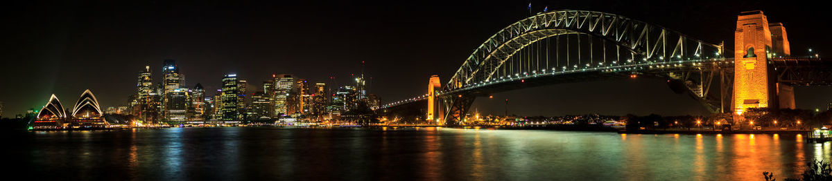 Panoramic view of illuminated bridge by city over sea against sky at night
