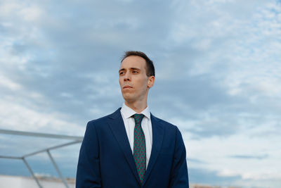 Young businessman in a suit and tie looking away thoughtful outside with a cloudy sky