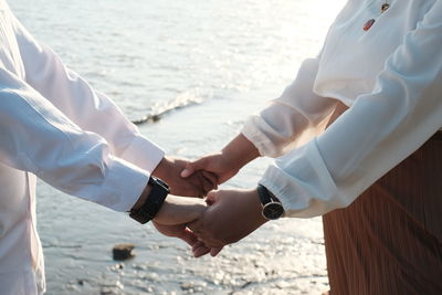 Midsection of couple holding hands at beach