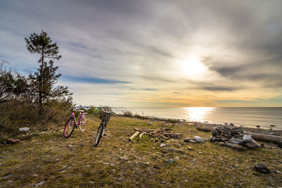 Man on bicycle by sea against sky during sunset