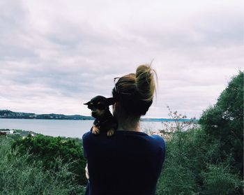 Rear view of woman holding dog against lake