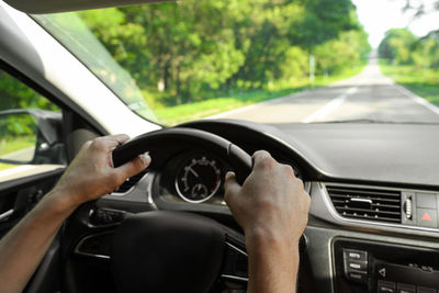 Male hands hold the steering wheel of a car while driving, inside view. close-up of the car interior