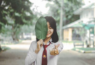 Cheerful woman holding leaf while standing on road in city