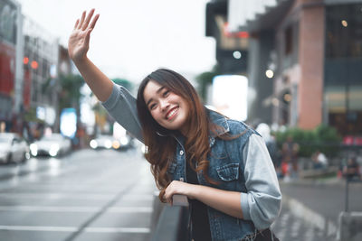 Portrait of smiling young woman gesturing while standing in city