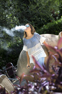 Woman exhaling smoke against trees