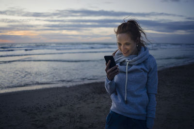 Woman using smartphone on the beach at sunset