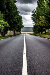 Empty road amidst trees against sky