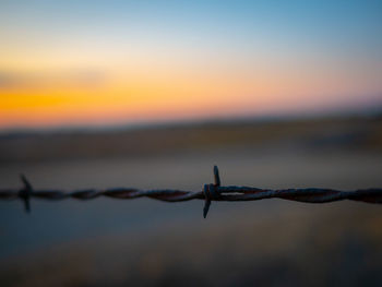 Close-up of barbed wire fence against sky during sunset