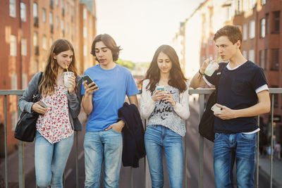 Teenagers using smart phone while drinking juice on bridge in city