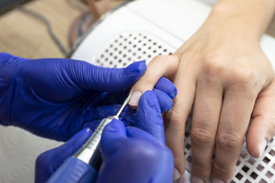 The manicurist cuts the cuticles of the nails with an electric milling machine wearing blue latex