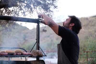 Side view of man preparing food on barbecue