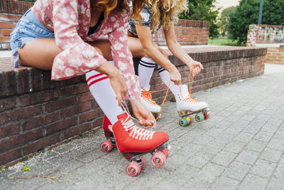 Women sitting on wall tying lace of roller skates