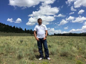 Portrait of confident man standing on field against sky