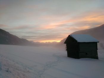 House on snowcapped mountain against sky during sunset