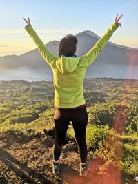 Rear view of woman with arms raised standing on land