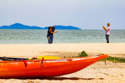 Close-up of moored canoe with friends enjoying at beach in background
