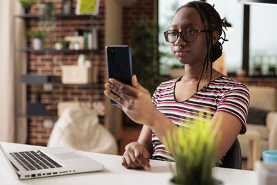 Young woman using phone while sitting on table