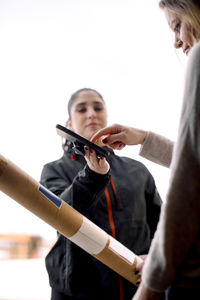 Female customer signing on mobile phone while receiving package from delivery woman