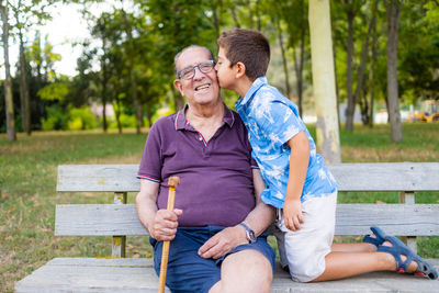 Gradson kissing his grandfather sitting on a bench in the park