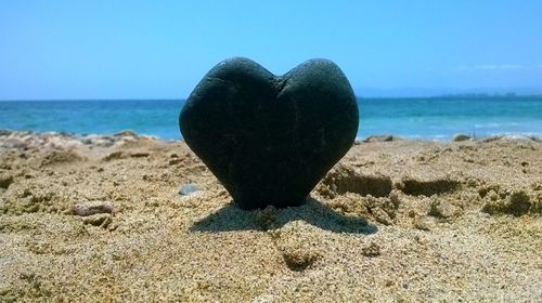 Close-up of heart shape on sand at beach against clear sky