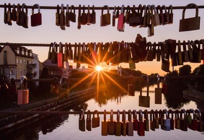 Locks hanging on railing over river against sky during sunset