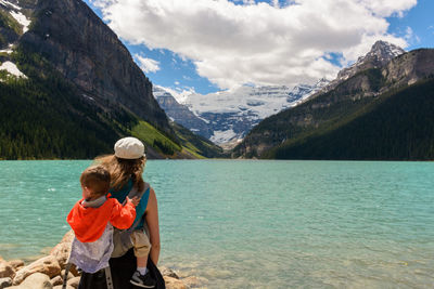 Rear view of mother and son standing by lake against mountains