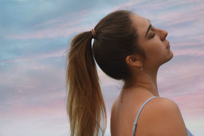 Portrait of young woman looking away against sky