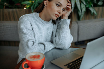 Tired young woman working on a laptop in a cafe