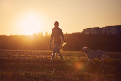 Full length of woman with dog on field during sunset