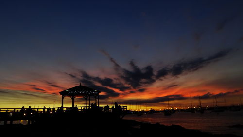 Silhouette built structure on beach against sky at sunset