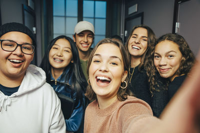 Cheerful teenage classmates taking selfie in corridor