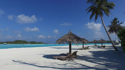 Lounge chairs by swimming pool at beach against sky