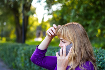 Caucasian blond woman talking on the phone outside, outdoor. 40s years old woman in purple blouse 