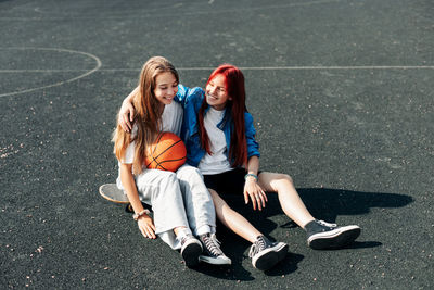 A couple of teenage girls on a sports street court with a basketball lifestyle relax after 