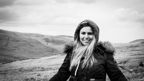 Portrait of smiling young woman standing on mountain against sky
