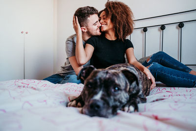 Laughing couple sitting on bed with dog at home