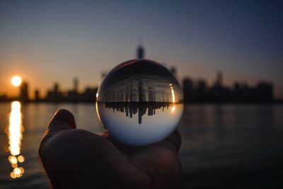 Person holding crystal ball against sky during sunset